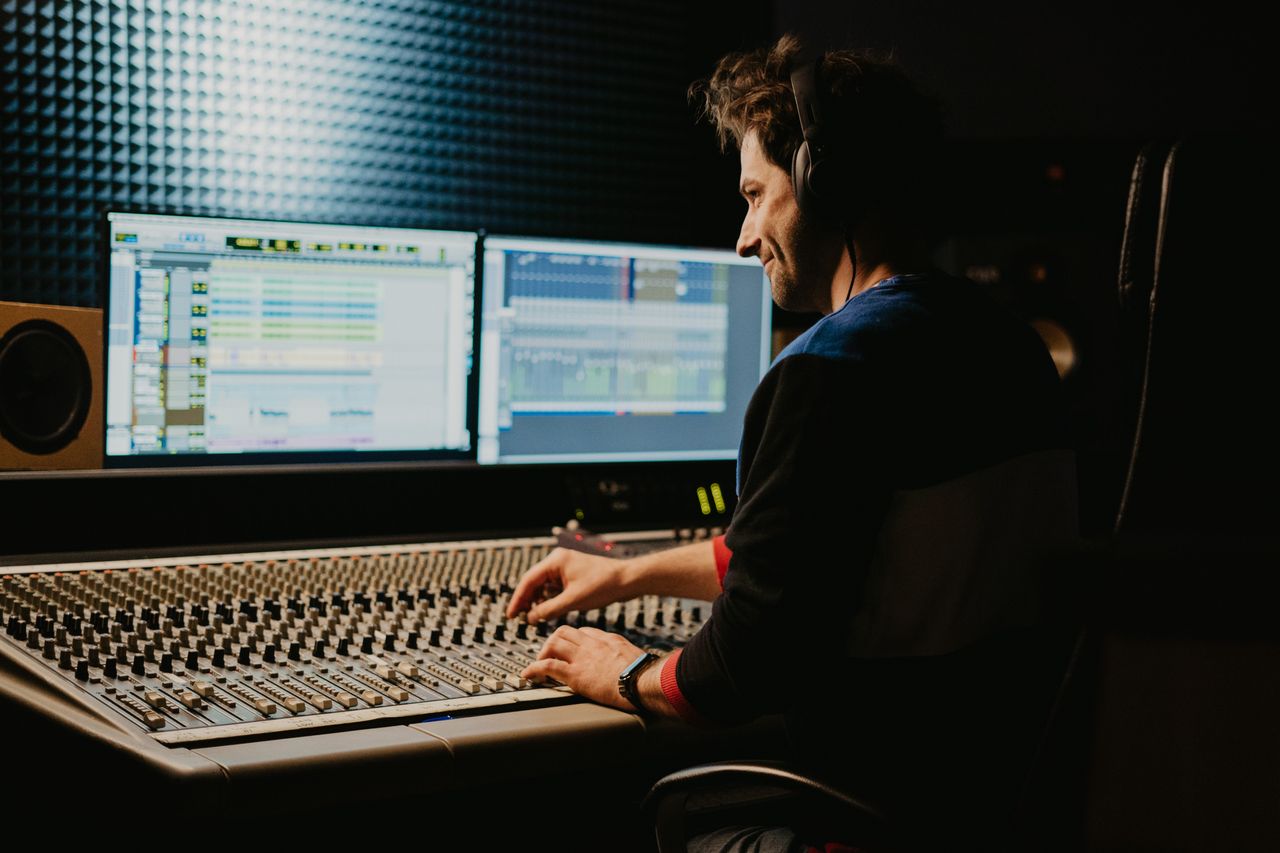 A sound engineer using a mixing console in a recording studio, wearing headphones and adjusting controls.